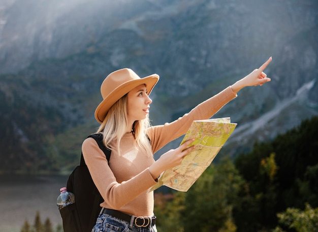Фото Страсть к путешествиям и концепция путешествий. стильная девушка путешественника в шляпе, глядя на карту, изучает лес. молодой оман с рюкзаком, путешествуя по озеру в лесу.