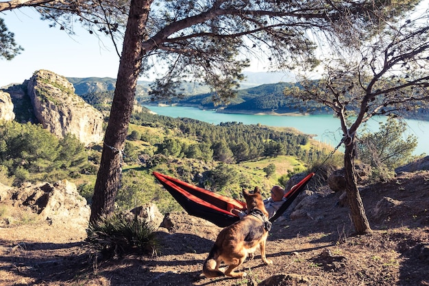 Wanderlust man and dog relaxing at hammock in mountains