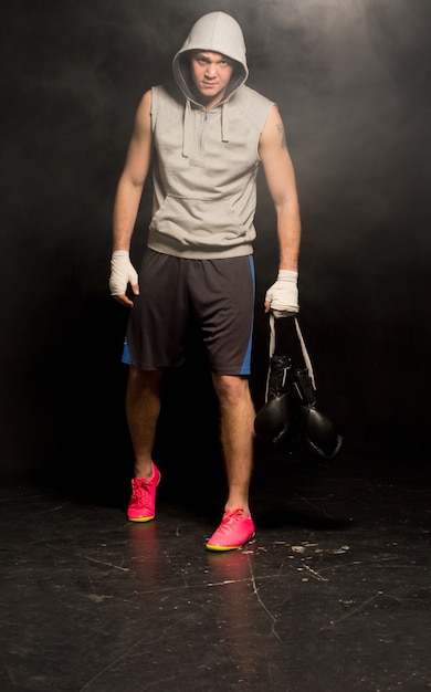 Wanhopige jonge bokser vertrekt na een nederlaag met een hoodie en zijn handschoenen in zijn verbonden handen