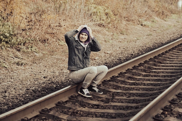 Wanhopige man zit op de spoorweg Zijaanzicht van hopeloze man in casual outfit die zijn hoofd aanraakt terwijl hij op rails zit in het herfstlandschap