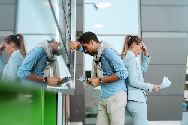 Wanhopige twee zakenmensen die niet op hun werk zijn Ze staan buiten voor het zakencentrum en houden papierwerk en een tablet vast.