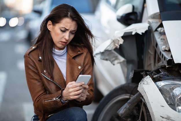 Wanhopige vrouw typt op mobiele telefoon terwijl ze na het ongeval naast haar vernielde auto was