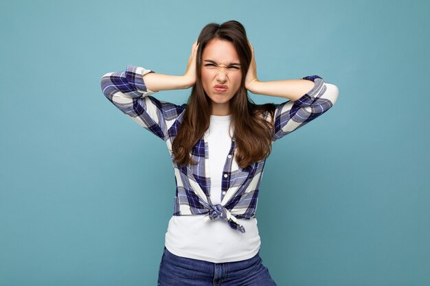 Don't want to hear it. Young emotional dissatisfied beautiful brunette woman wearing check shirt isolated on blue