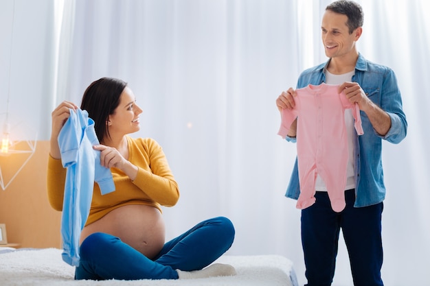 Want little girl. Smiling brunette pregnancy crossing legs while sitting on the bed and looking aside