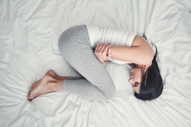 Want to sleep. Top view of charming brunette girl that crossing arms on chest while lying on her bed