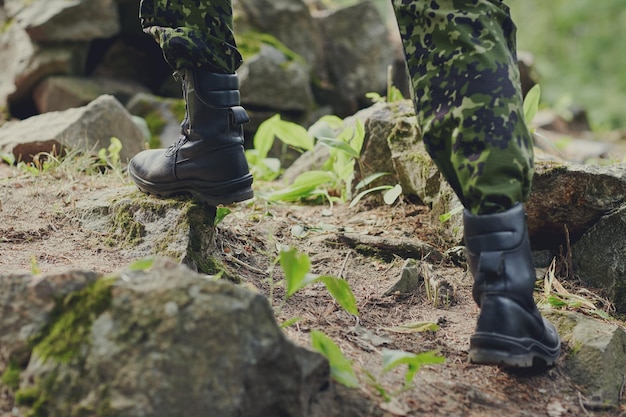 戦争、ハイキング、軍隊と人々の概念-森の岩に登る兵士の足のクローズアップ