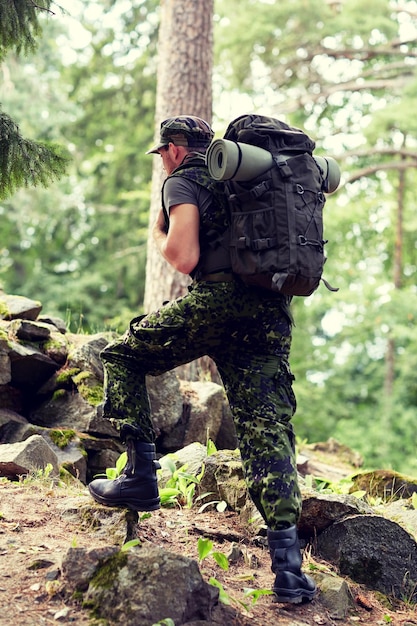 戦争、ハイキング、軍隊、人々の概念-森の中を歩くバックパックを持つ若い兵士またはレンジャー