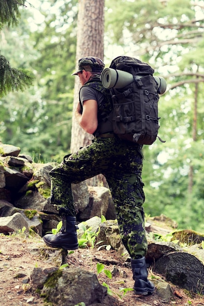 war, hiking, army and people concept - young soldier or ranger with backpack walking in forest