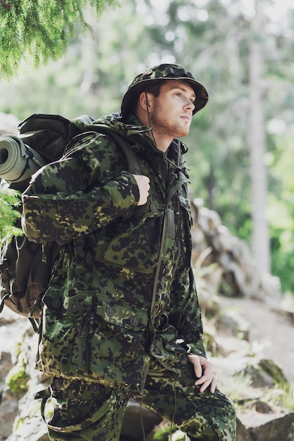 war, hiking, army and people concept - young soldier or ranger with backpack walking in forest