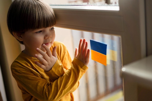 Photo war in ukraine the baby looks out the window with the flag of ukraine