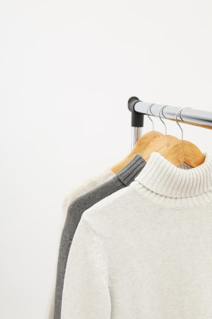 Wardrobe rack with hangers with sweaters on light background