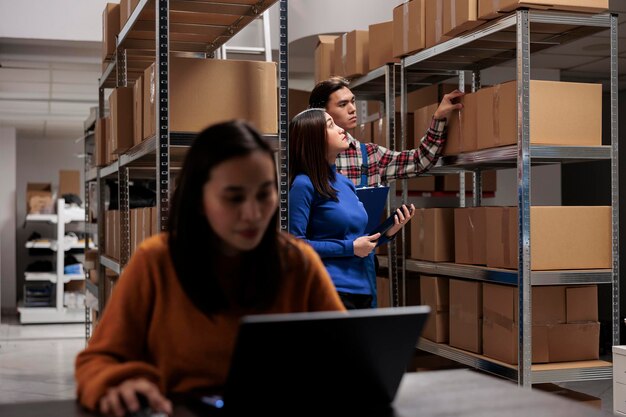 Warehouse asian managers team processing customer order and searching box on shelf. Storehouse package handler and supervisor inspecting goods parcels on rack in storage room