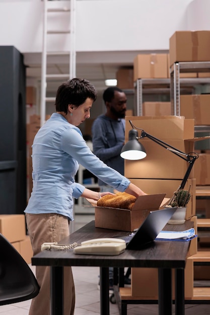 Warehouse employee putting trendy clothes in carton boxes preparing packages for delivery, after checking shipping details working in storehouse. Worker analyzing transportation logistics