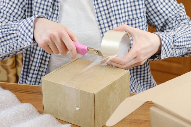 Photo warehouse employee wraps the order of online store with scotch tape in cardboard box