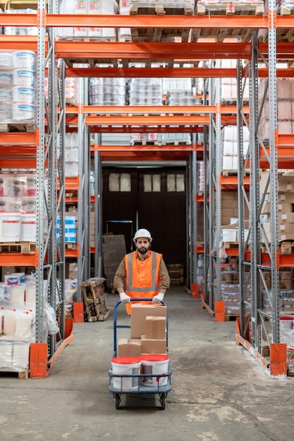 Warehouse engineer in workwear moving forwards between racks