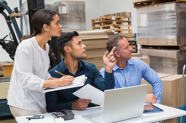 Warehouse manager pointing something to his colleagues in a large warehouse