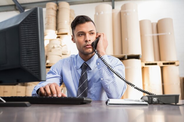 Warehouse manager using cellphone and laptop