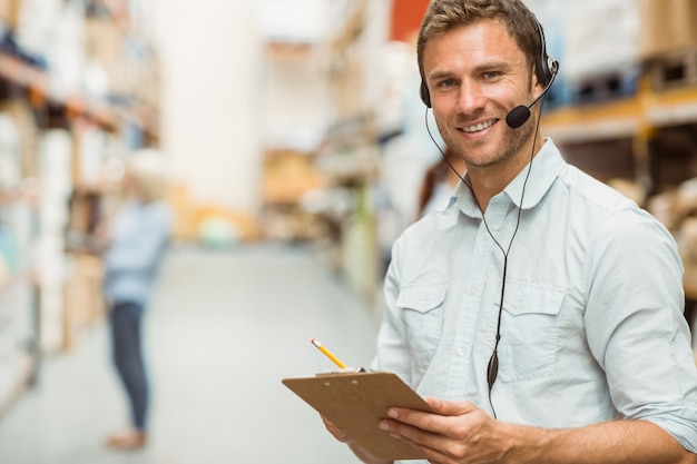 Photo warehouse manager wearing headset writing on clipboard