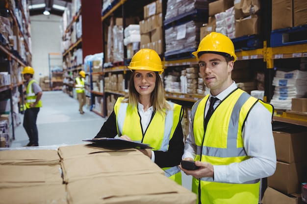 Warehouse managers looking at clipboard with helmets