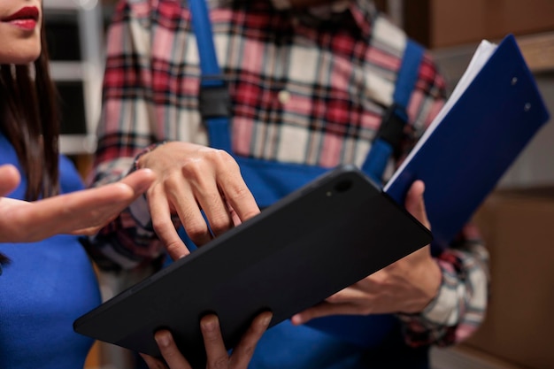 Photo warehouse operators checking inventory data on digital tablet and analyzing orders checklist on clipboard. storehouse postal managers colleagues comparing quality control reports