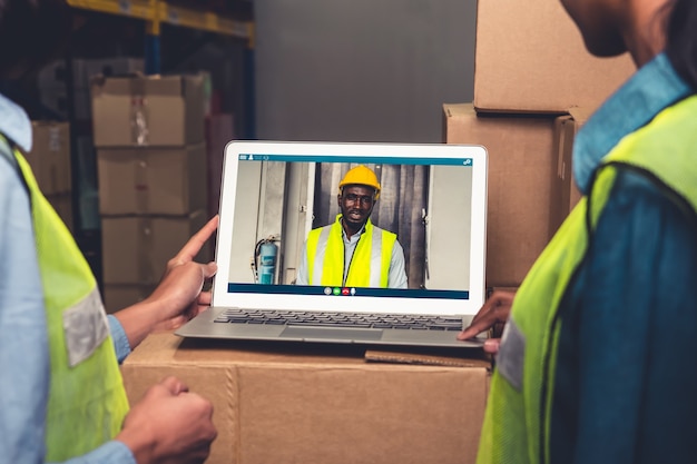 Warehouse staff talking on video call at computer screen in storage warehouse