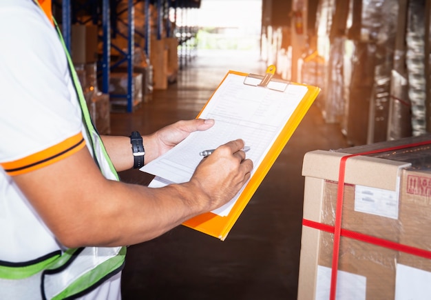 Warehouse worker holding clipboard his doing inventory management cargo boxes. Checking stock, Cargo shipment, Warehousing storage.