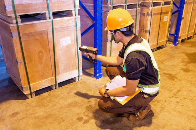 Scanner del codice a barre di scansione del lavoratore del magazzino sul pallet pesante della cassa nel magazzino di stoccaggio