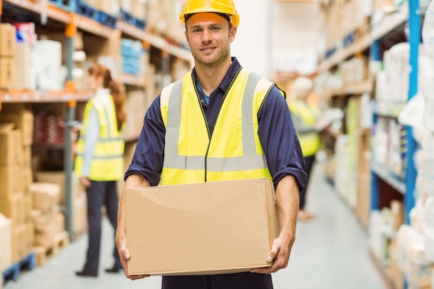 Warehouse worker smiling at camera carrying a box