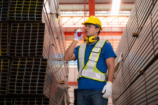 Warehouse workers in hard hats and helmets stand in the warehouse to count and inspect the steel