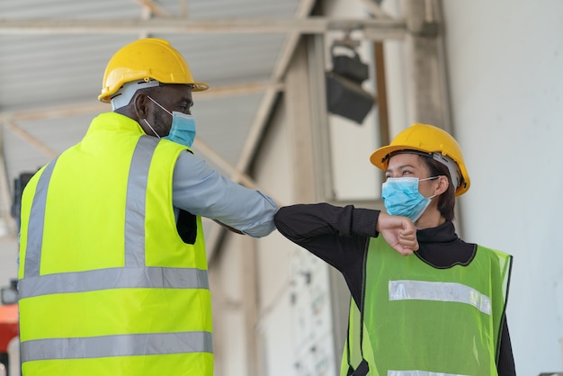 ロジスティクス倉庫工場でコロナウイルスの挨拶のぶつかる肘を保護するためのフェイスマスクを身に着けている倉庫作業員