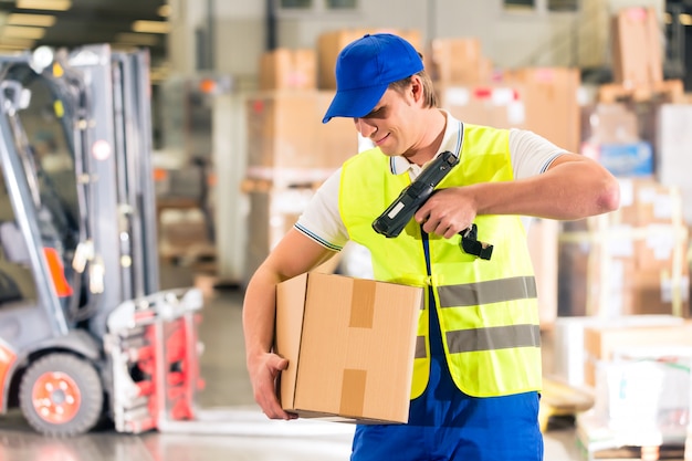 Warehouseman met beschermend vest en scanner, scant streepjescode van pakket, hij staat in magazijn van expeditiebedrijf