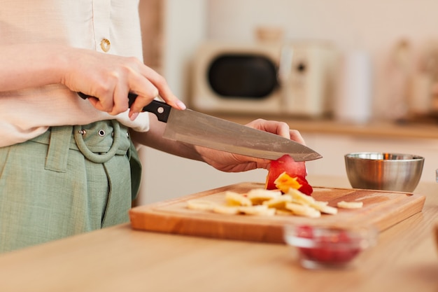 Warm afgezwakt close-up van onherkenbaar vrouw fruit snijden tijdens het maken van een gezond ontbijt in de keuken