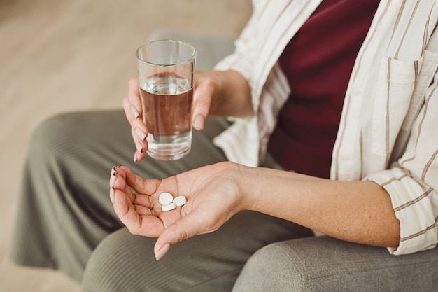 Warm afgezwakt close-up van onherkenbare vrouw met pillen en glas water, medicijnen en herstelbehandeling, kopie ruimte