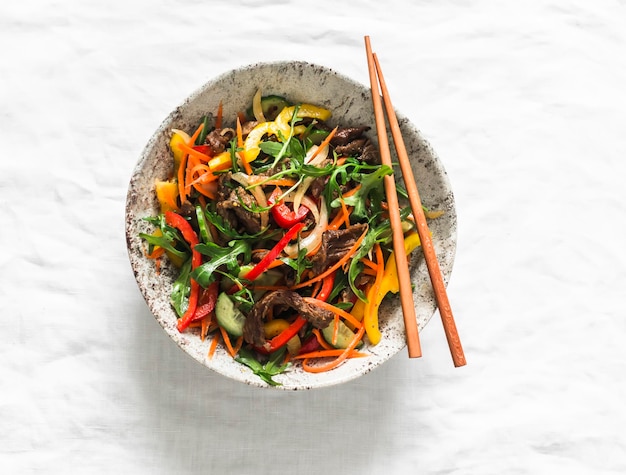 Warm asian style salad with beef and vegetables on a light background top view