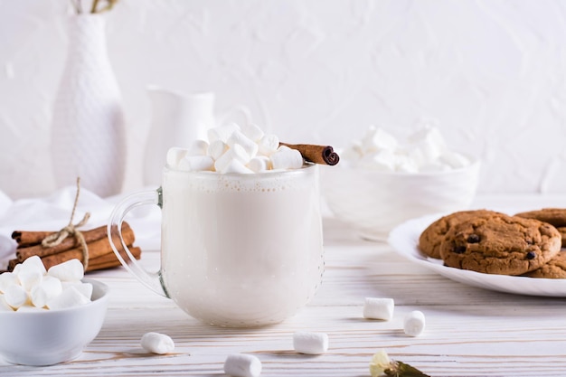 Warm cocoa with marshmallows and cinnamon in a cup and a plate of oatmeal cookies on the table