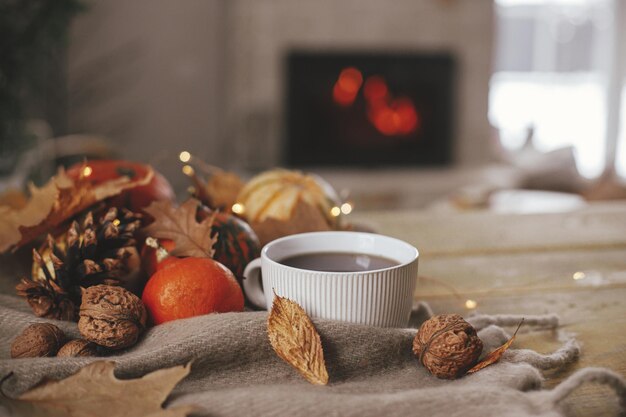 Warm cup of tea pumpkins autumn leaves cones cozy scarf and lights on rustic wooden table in farmhouse Fall in rural home Happy Thanksgiving Fall hygge still life copy space