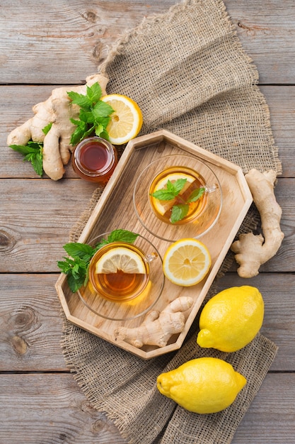 Photo warm drink beverage infusion in glass for cold flu winter fall days. cup of ginger tea with mint, lemon and honey on a wooden table, flat lay