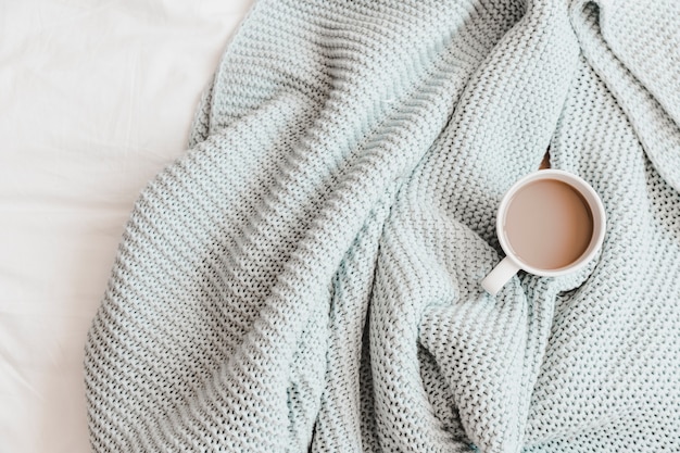 Warm drink in knitting blue plaid on bedsheet