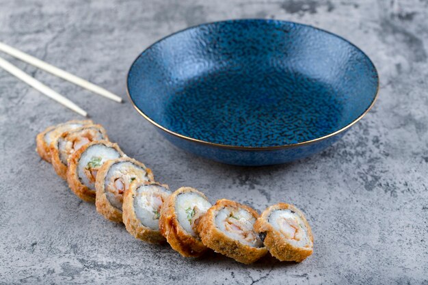 Warm gebakken sushi rolt met houten wegwerp eetstokjes op stenen tafel.