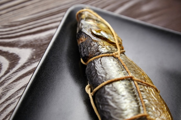 Warm gerookte vis, kippeharing. Twijn gebonden vis op zwarte plaat op bruin houten tafel, close-up