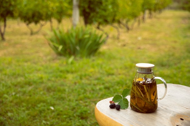 Warm glass teapot, green tea leaves and lemongrass on the wooden desk in plantations, empty space for text.