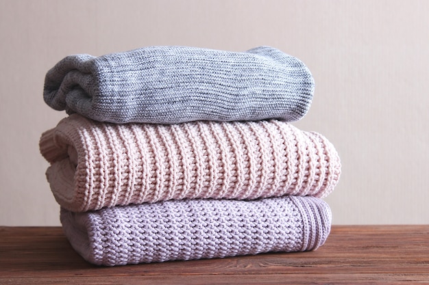 Warm knitted sweaters folded in a stack on a light background closeup