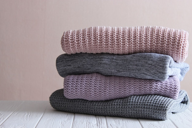 Warm knitted sweaters folded in a stack on a light background closeup