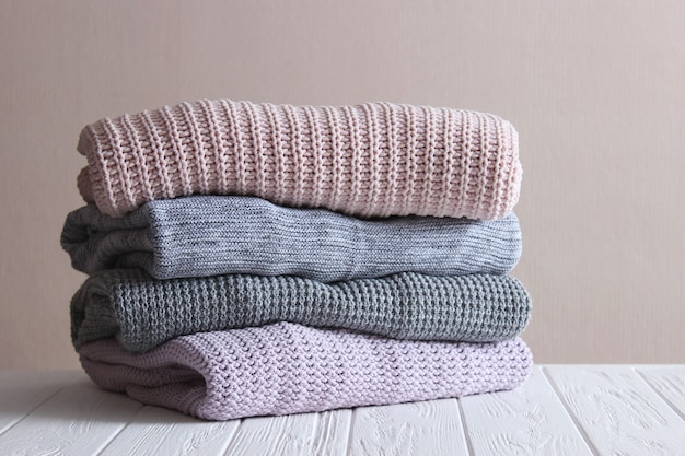 Warm knitted sweaters folded in a stack on a light background closeup