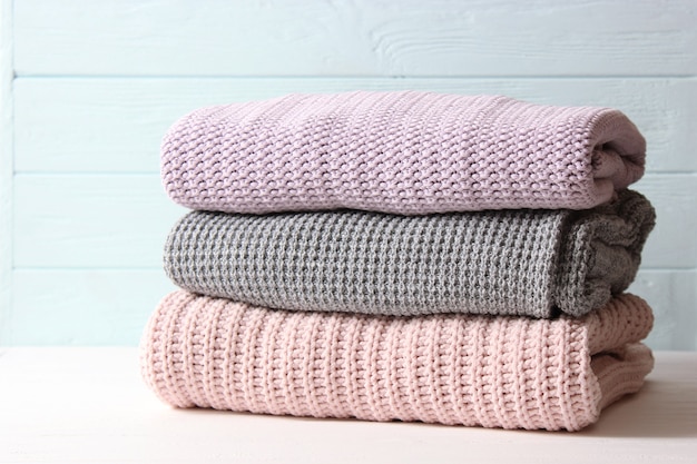 Warm knitted sweaters folded in a stack on a light background closeup