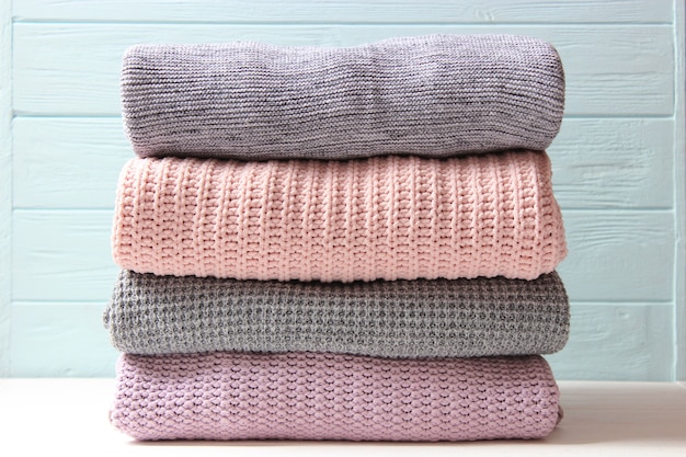 Warm knitted sweaters folded in a stack on a light background closeup