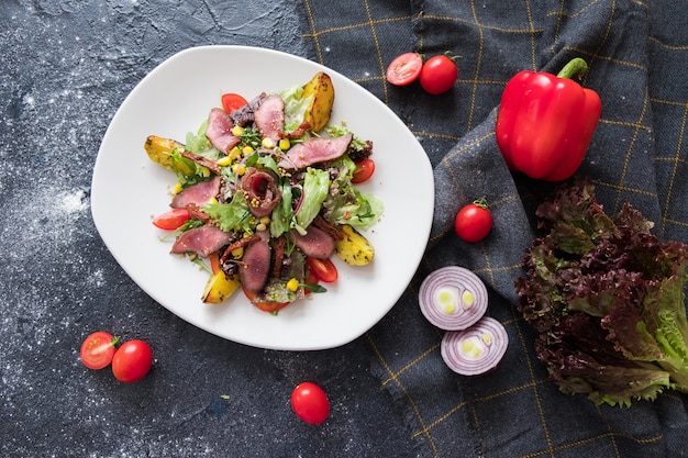 Warm meat salad with arugula on white plate on dark stone background. 