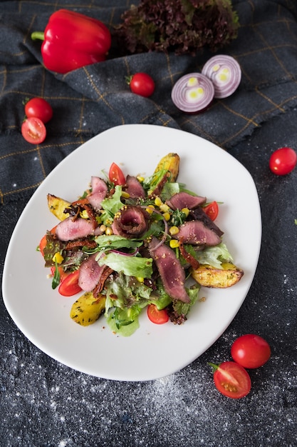 Warm meat salad with arugula on white plate on dark stone background. 