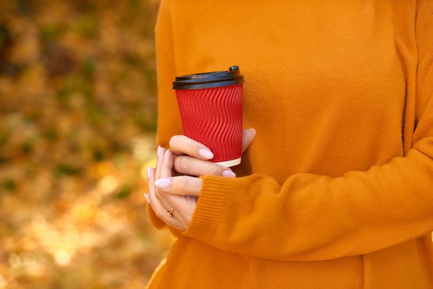 オレンジ色の黄色の落ち葉を背景に手でホット コーヒーのクラフト カップの暖かい写真