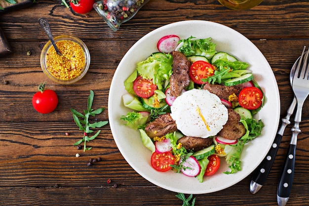 Warm salad from chicken liver, radish, cucumber, tomato and egg poached. Healthy food. Top